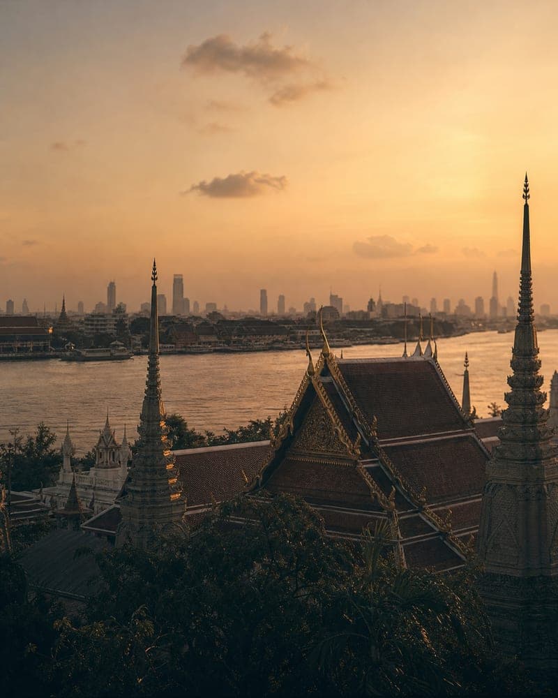 Bangkok am Fluss in warmer Abendstimmung mit Tempeldächern